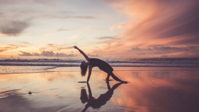 kvinde dyrker yoga i solnedgangen på en strand